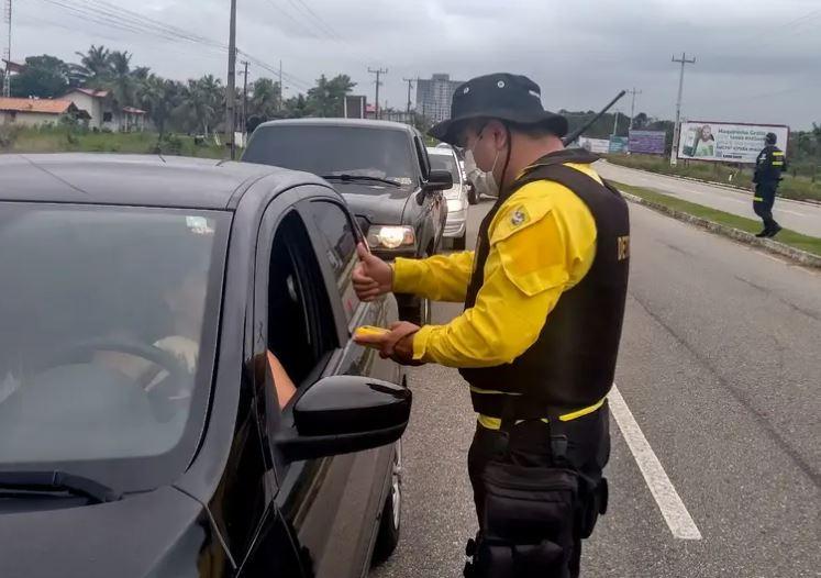 A imagem em destaque mostra um agente de trânsito do Detran durante fiscalização ao condutor de um carro.